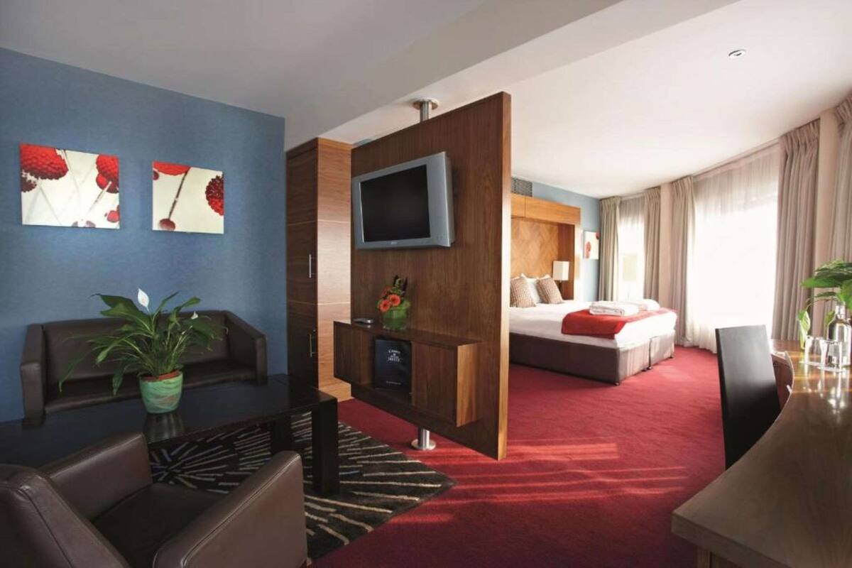 A hotel room with a TV, a bed, a sofa, a coffee table, and a plant.