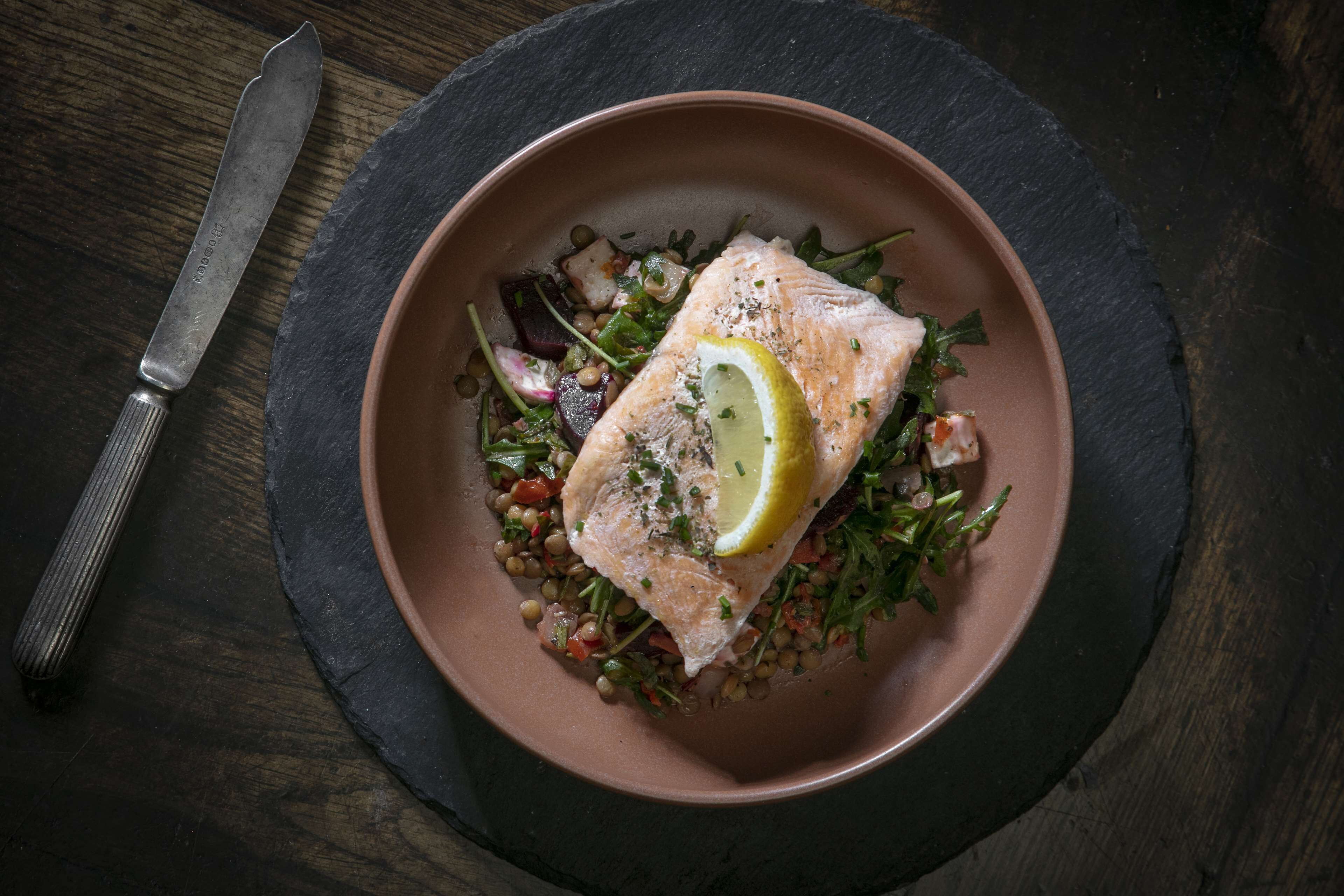 A salmon dish with lemon and greens on a plate.