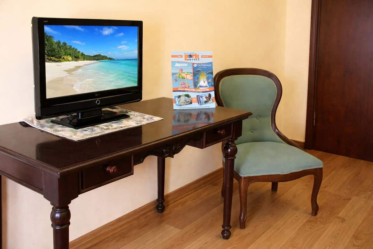 A wooden desk with a television, a chair, and a travel magazine on it.