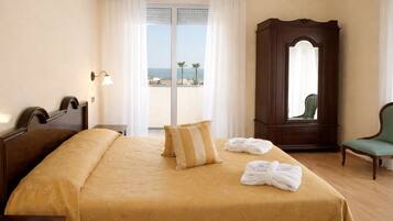 Habitación de hotel con cama, un espejo grande, una silla verde y vista al mar a través de la ventana.