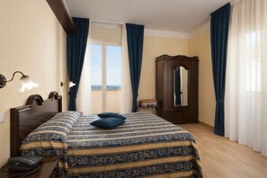 Een hotelkamer met een bed, een houten kledingkast, een telefoon op het nachtkastje en uitzicht op zee door een groot raam.