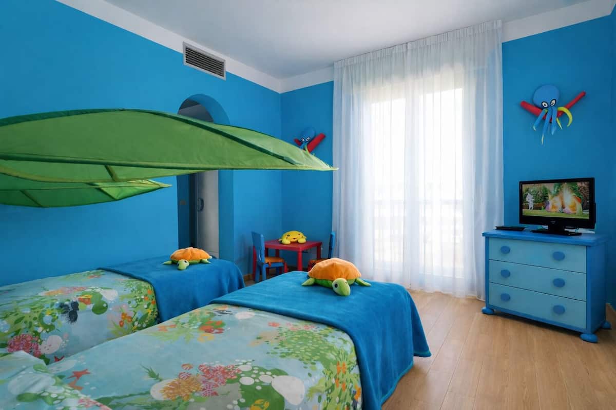 A room with two beds, a TV, a desk, and a window with curtains.