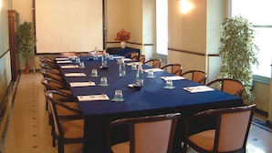 A conference room with a long table, chairs, a projector screen, and potted plants.