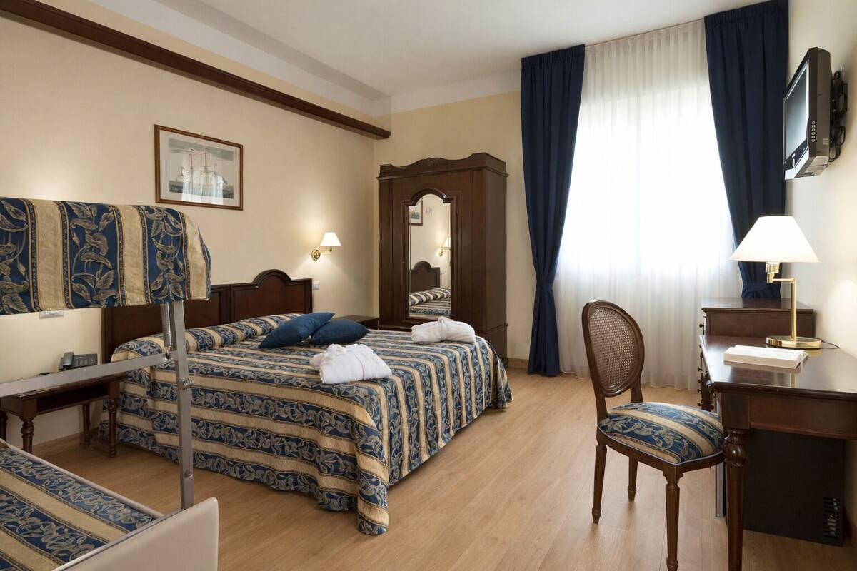 A hotel room with a bed, a desk, a chair, a mirror, a television, and a window with curtains.