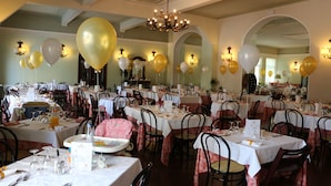 A banquet hall with multiple tables set for dining, featuring chandeliers and wall sconces.