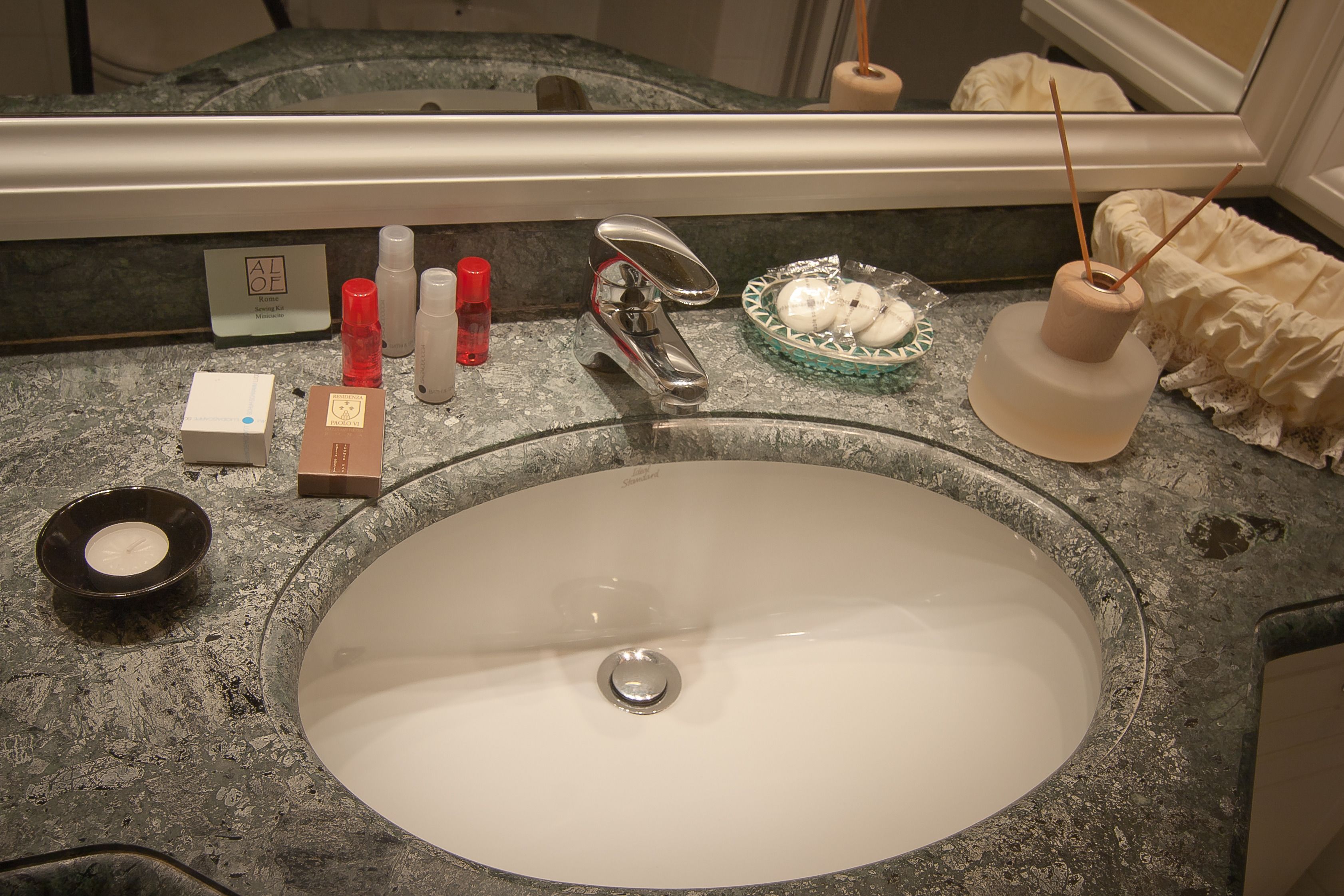A bathroom sink with a mirror above it, a soap dispenser, a toothbrush holder, and a glass bowl with soap.