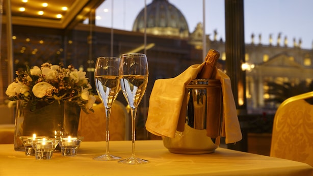 A table with two champagne flutes, a vase with flowers, and a candle holder. - Residenza Paolo VI (Rome)