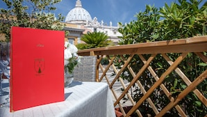 A red menu with "RESIDENZA PAOLO VI" on a table outdoors with a view of a historic building. - Residenza Paolo VI (Rome)