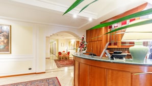 A reception area with a wooden counter, a red carpet, and a framed painting on the wall. - Residenza Paolo VI (Rome)