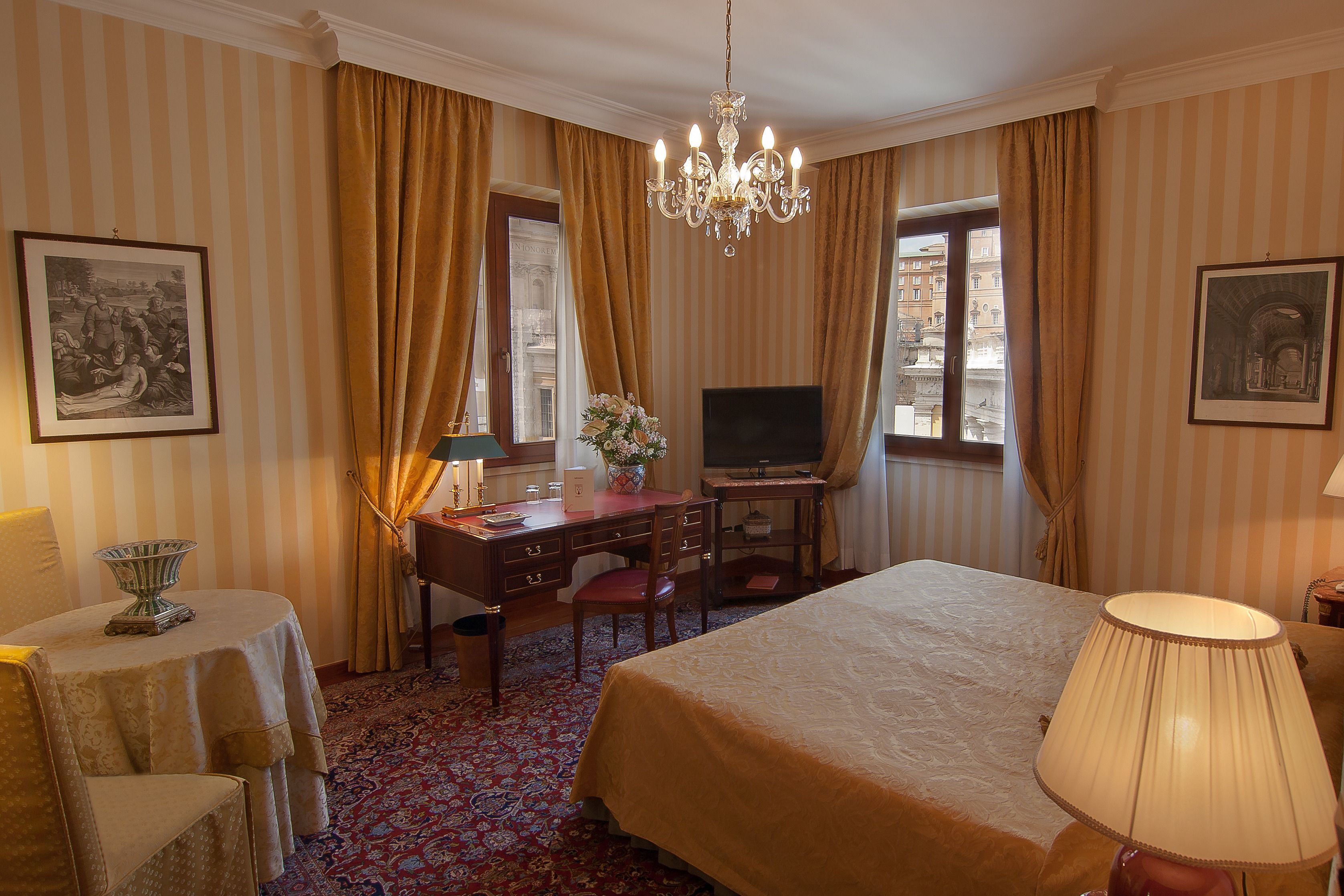 A hotel room with a bed, desk, television, and a chandelier.