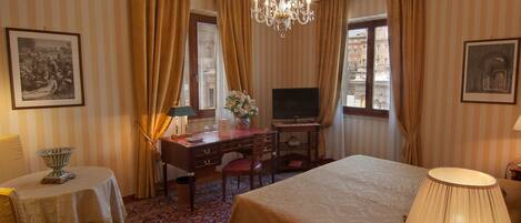A hotel room with a bed, desk, television, and a chandelier.