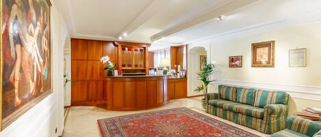 Un amplio salón con un tapiz grande, un sofá verde a rayas y un mostrador de recepción de madera.