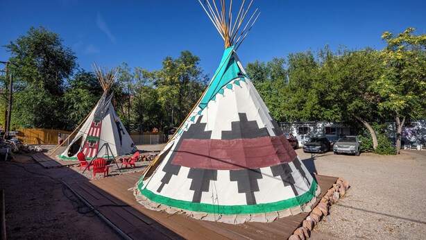 Deux tentes de style tipi, avec des chaises rouges devant, installées sur une terrasse en bois et bordées d’un chemin de gravier.