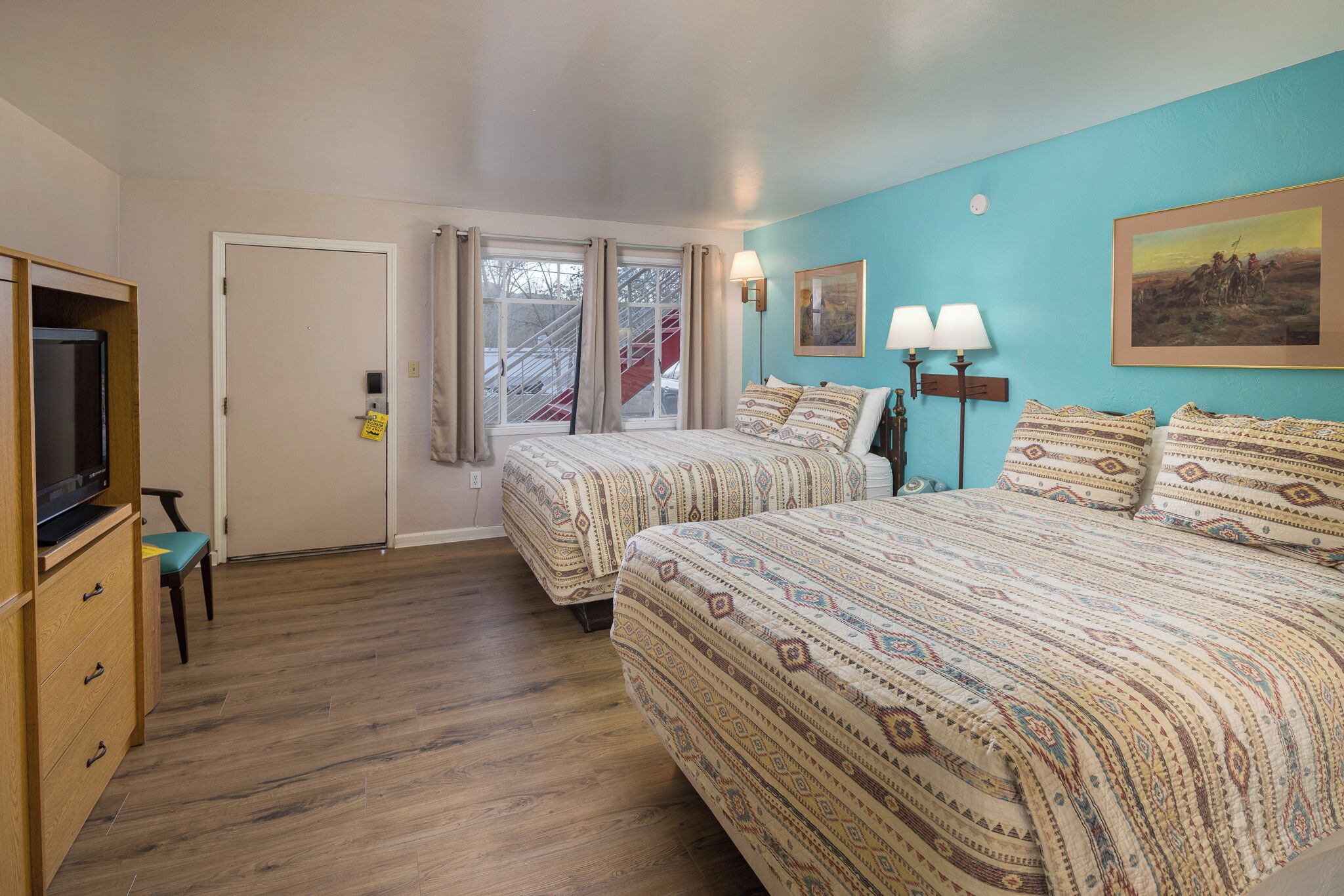 A bedroom with two beds, a TV, and a window with curtains.