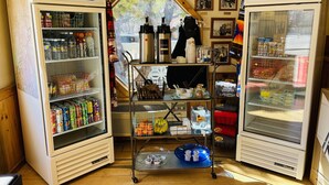 Une petite cuisine équipée comprenant deux mini-réfrigérateurs, une petite étagère avec des boissons et un chariot métallique contenant les ustensiles de cuisine essentiels.