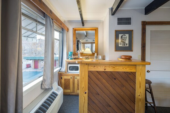 A compact kitchen with wooden cabinetry, a built-in microwave, and a window with curtains.