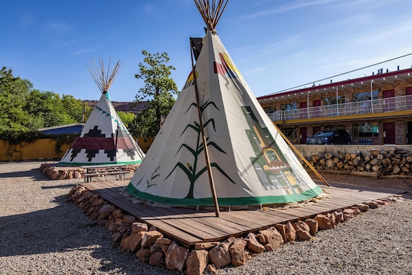 Dos tipis con plataformas de madera, frente a un edificio con balcón.