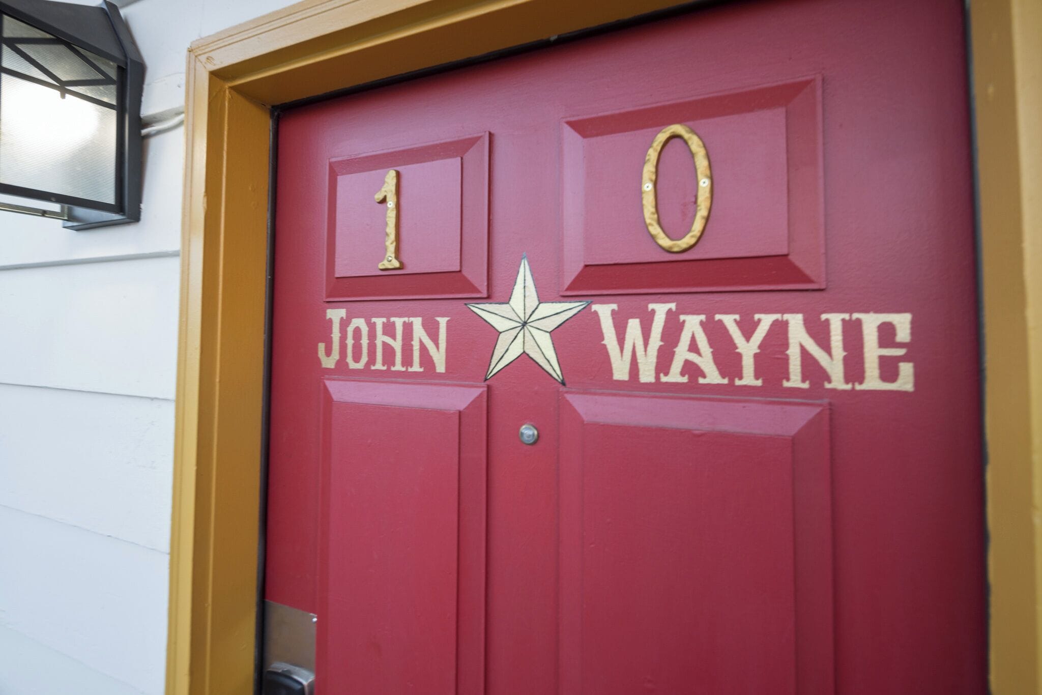 A red door with the number 10 and the name "John Wayne" in gold lettering, a star symbol, and a small window above the door.