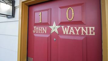 A red door with the number 10 and the name "John Wayne" in gold lettering, a star symbol, and a small window above the door.