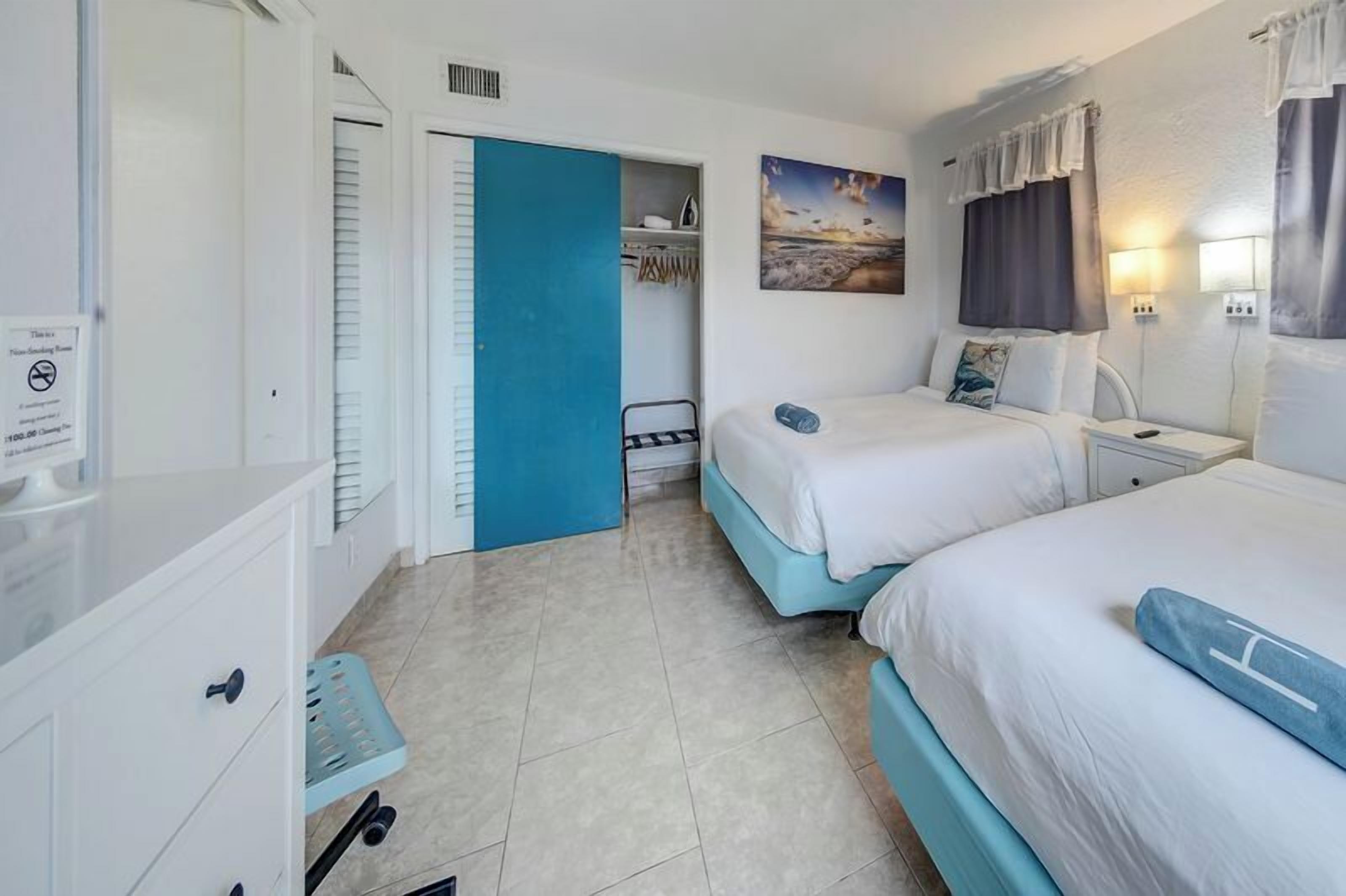 A hotel room with two beds, a wardrobe, a desk, and a bathroom.