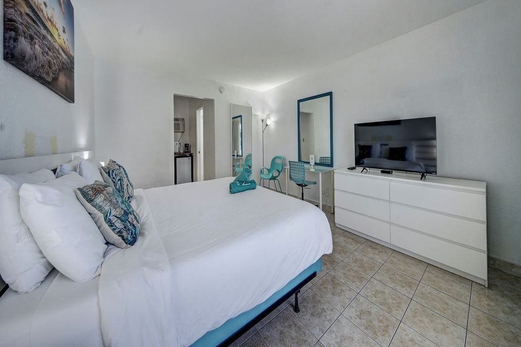 Un dormitorio con cama, cómoda, televisor y baño a la vista.