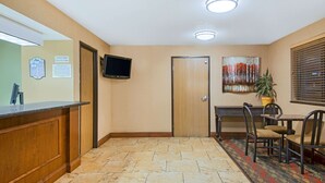 Un'area di accoglienza con una scrivania in legno, una TV a schermo piatto montata a parete, una porta chiusa e un piccolo tavolo con sedie.