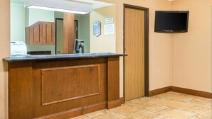 Un'area reception di un hotel con un bancone in legno, una televisione a schermo piatto montata a parete e una porta sulla destra.