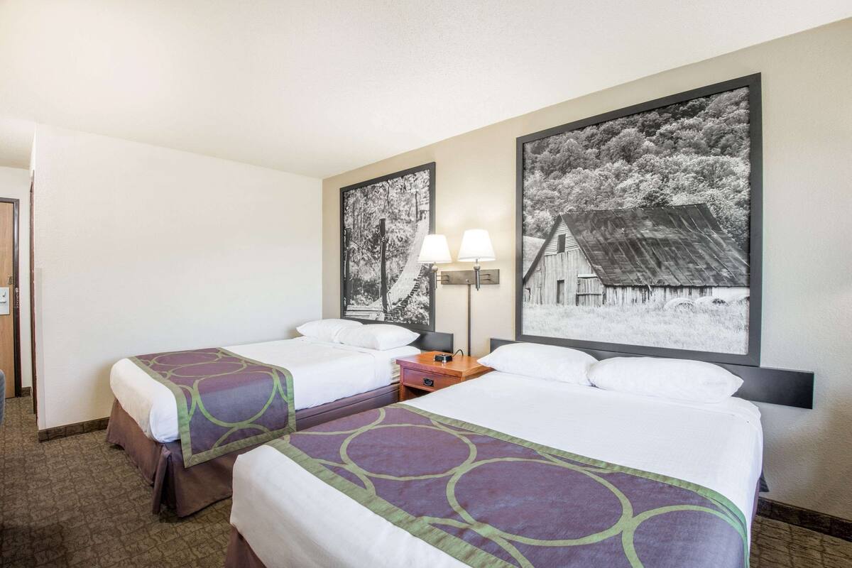 A hotel room with two beds, a nightstand, and two wall-mounted lamps.
