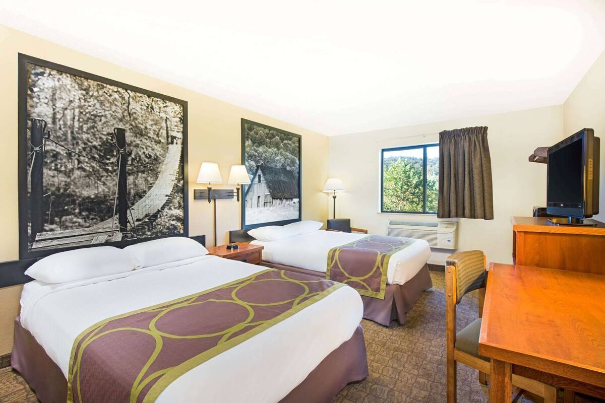 A hotel room with two beds, a desk, a television, and large framed pictures on the wall.