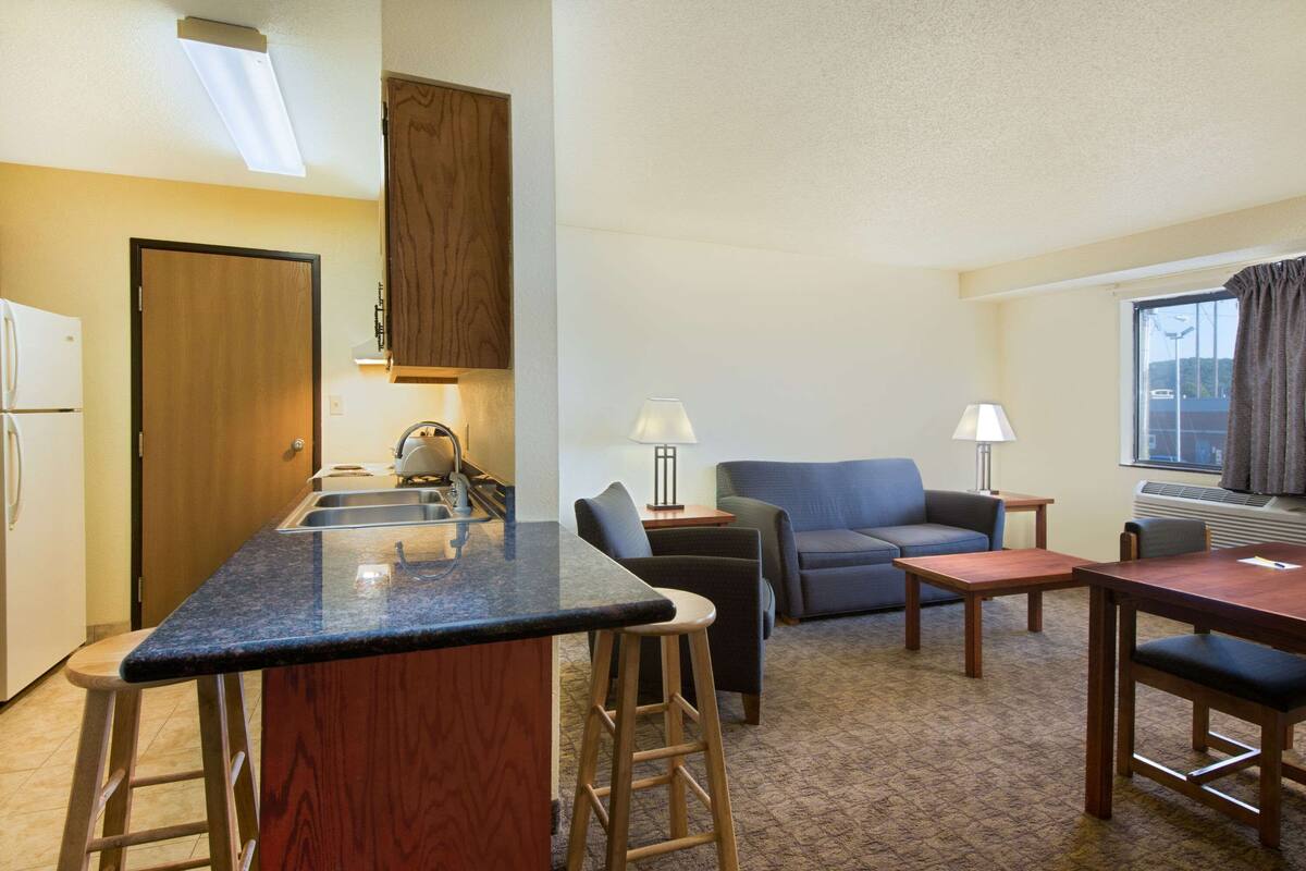 A compact living space with a kitchenette, a sofa, a dining table, and a bar stool.