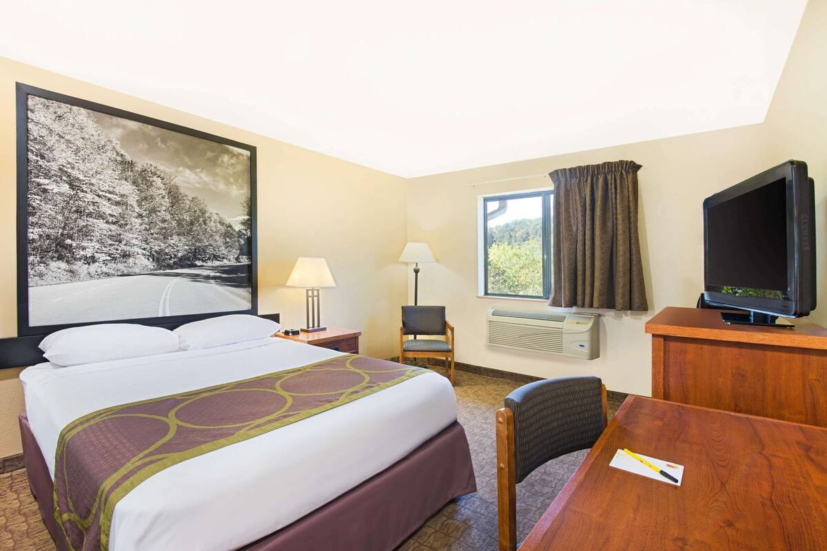 A hotel room with a large bed, a desk with a chair, a television, a window with curtains, and a painting on the wall.