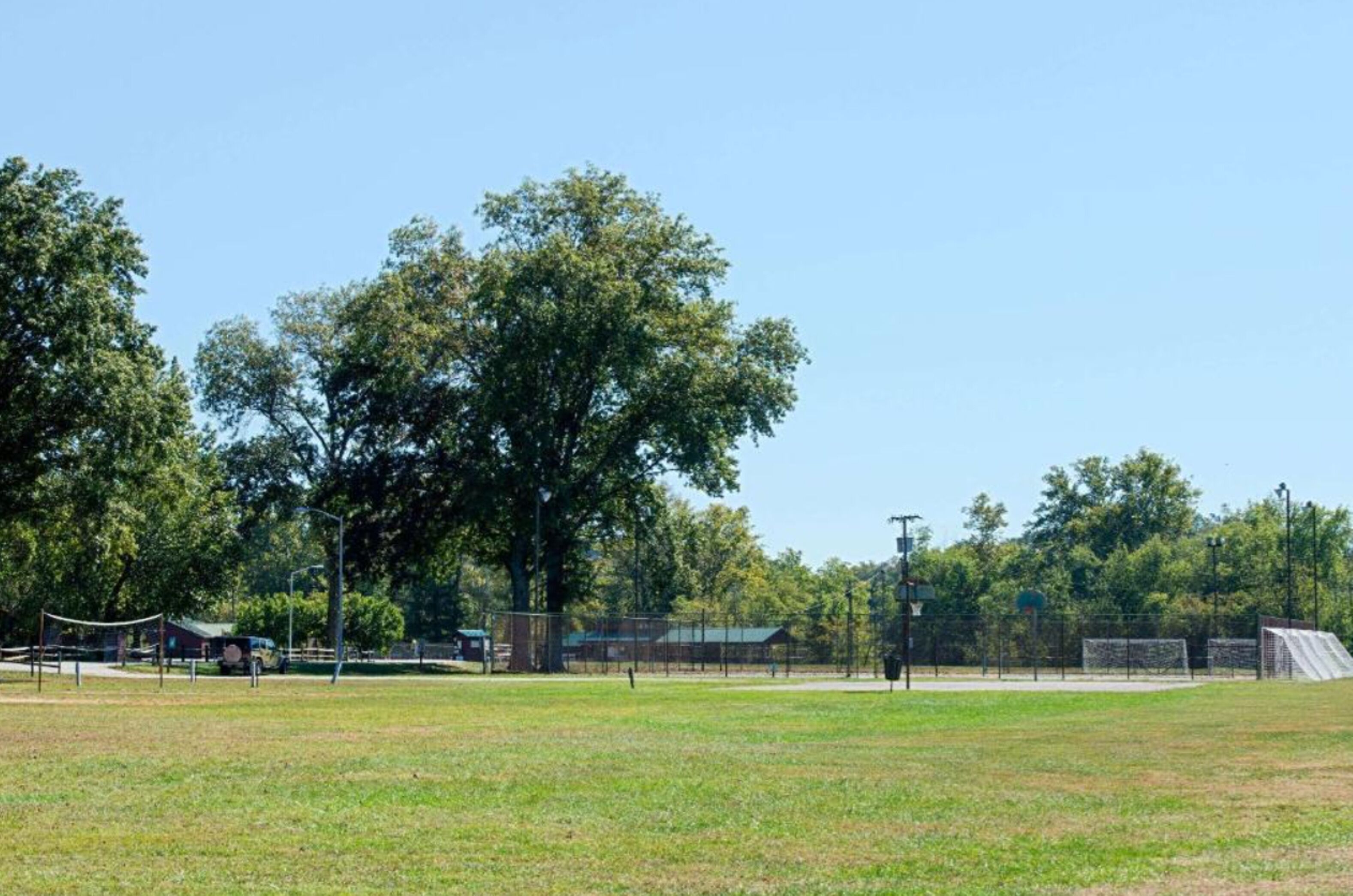 A sports field with a fence, trees, and a building in the background.