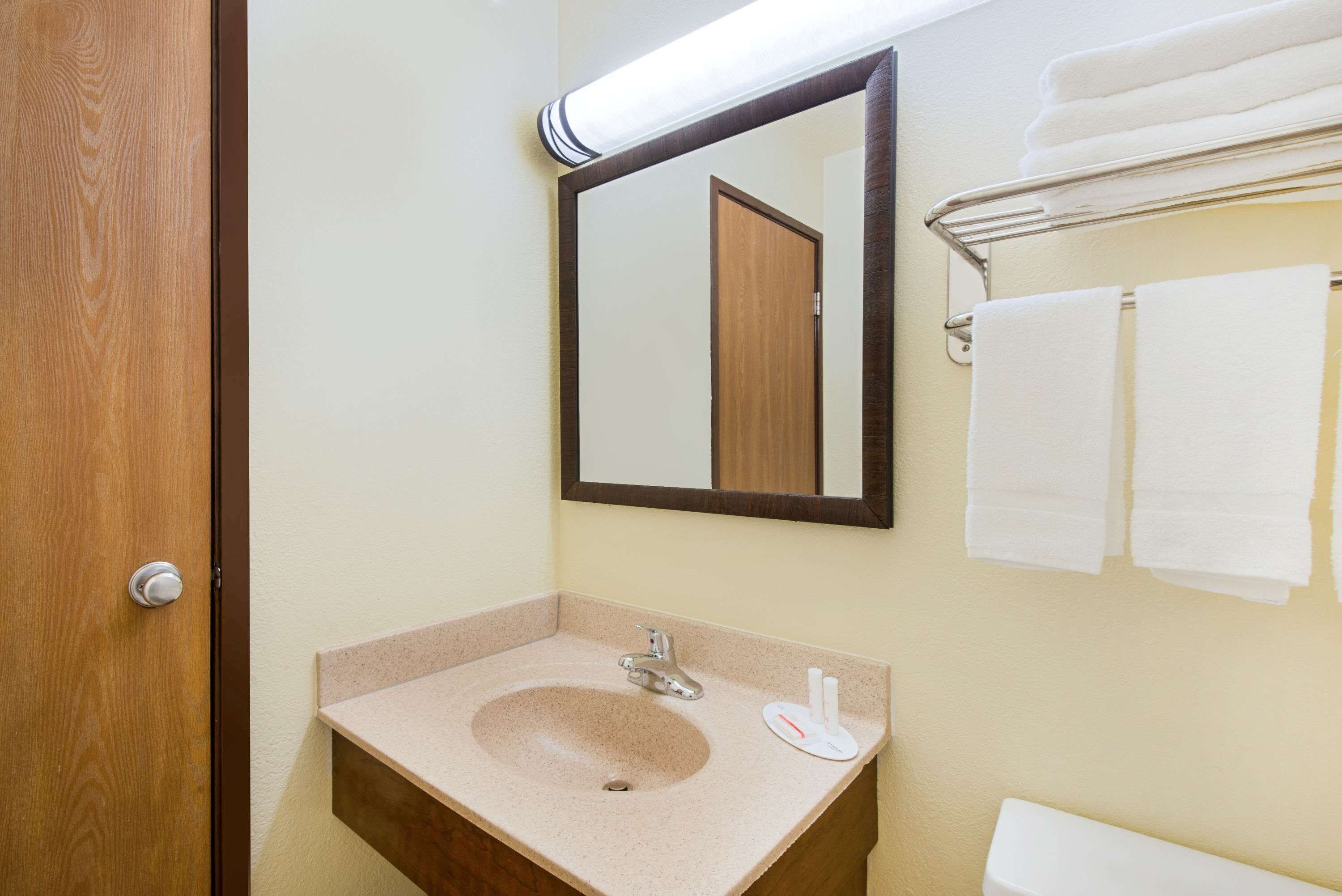 A bathroom with a wooden door, a sink with a mirror above it, and a towel rack with towels.