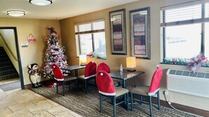 Una hall d'albergo con un albero di Natale, sedie rosse, un tavolo con una lampada e opere d'arte alle pareti.