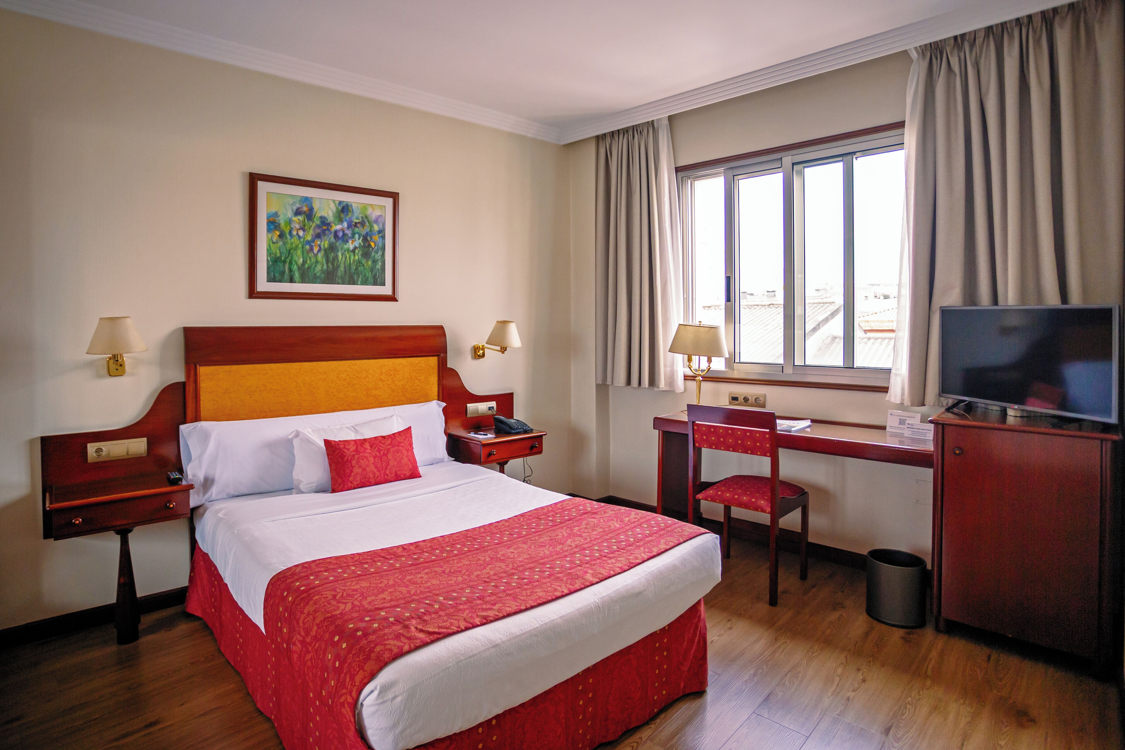 Habitación de hotel con una cama grande, un escritorio con silla, un televisor y una ventana con cortinas.