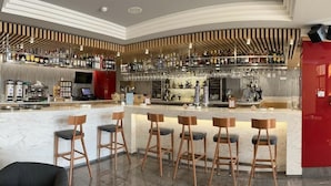 A modern bar area with a marble countertop, multiple bar stools, and a variety of bottles and glasses on shelves.
