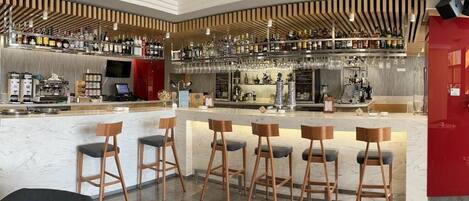 Un espace bar moderne doté d’un comptoir en marbre, de plusieurs tabourets et d’une variété de bouteilles et de verres disposés sur des étagères.