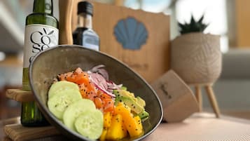 A bowl of fresh fruit salad with cucumber, mango, and red onion slices, accompanied by a bottle of olive oil and a wooden cutting board.