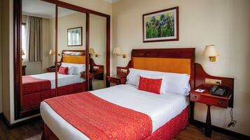 A hotel room with a large bed, a mirror, a painting, and a nightstand with a phone.