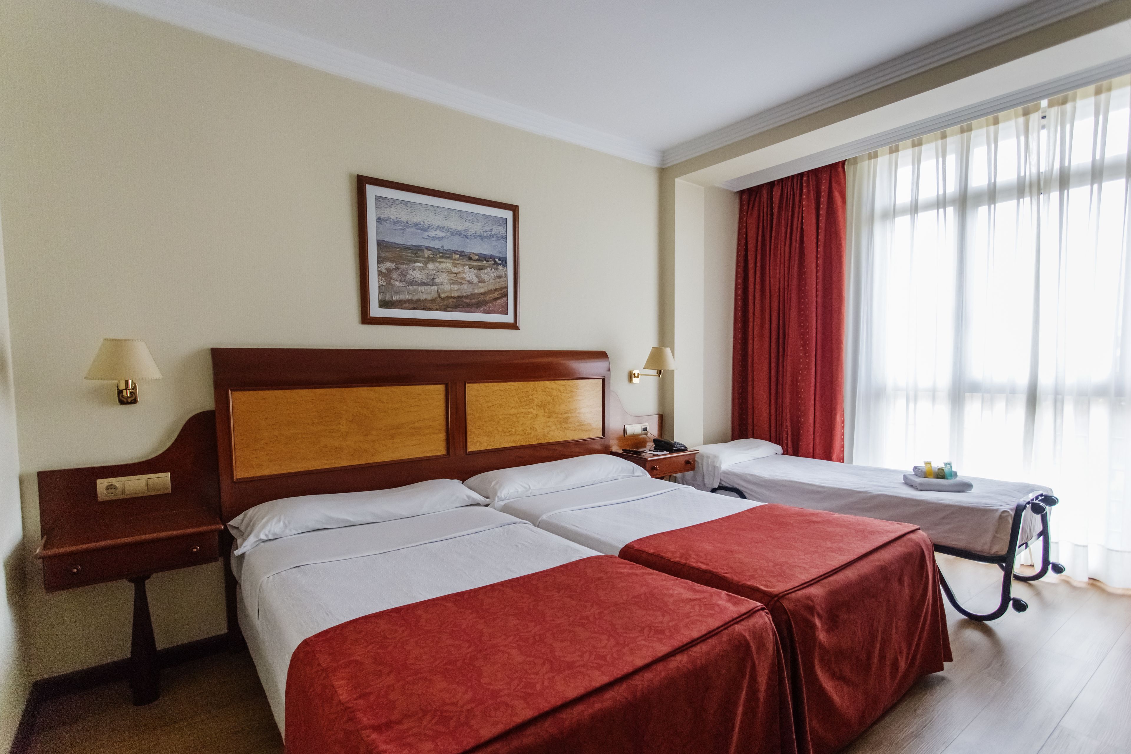 Habitación de hotel con dos camas, cabecera de madera, un cuadro en la pared y una ventana con cortinas.