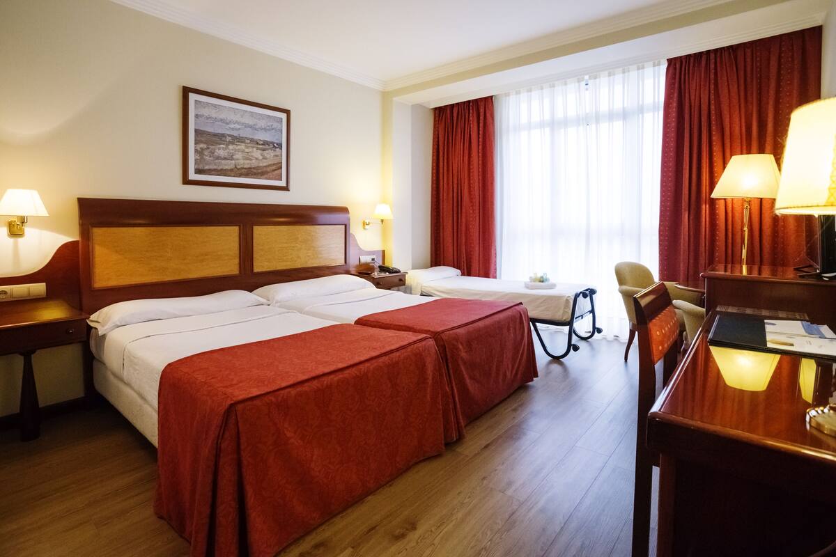 A hotel room with two beds, a desk, a chair, and a dining table.