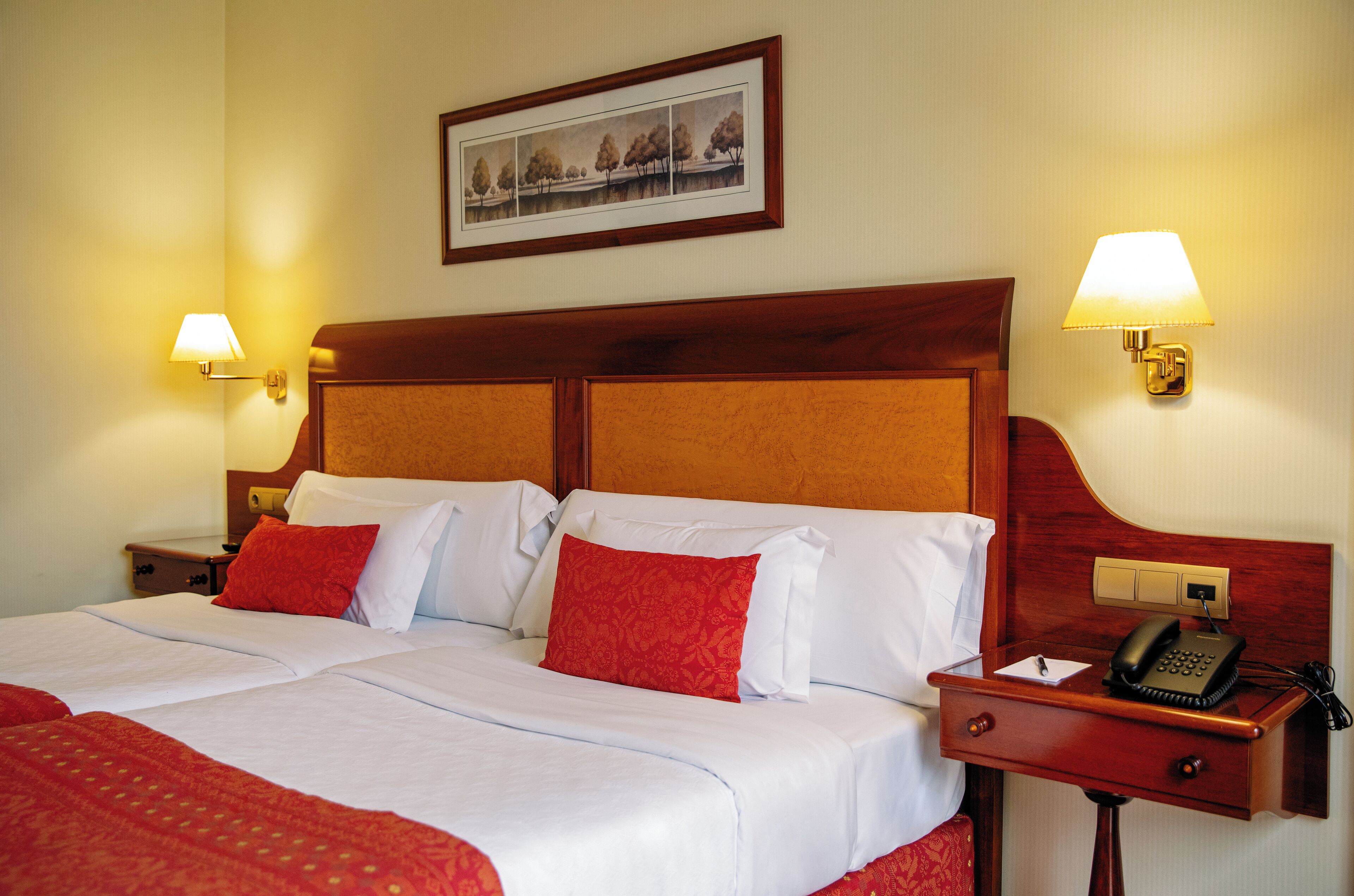 A hotel room with a large bed, two bedside lamps, a nightstand with a telephone, and a framed picture on the wall.