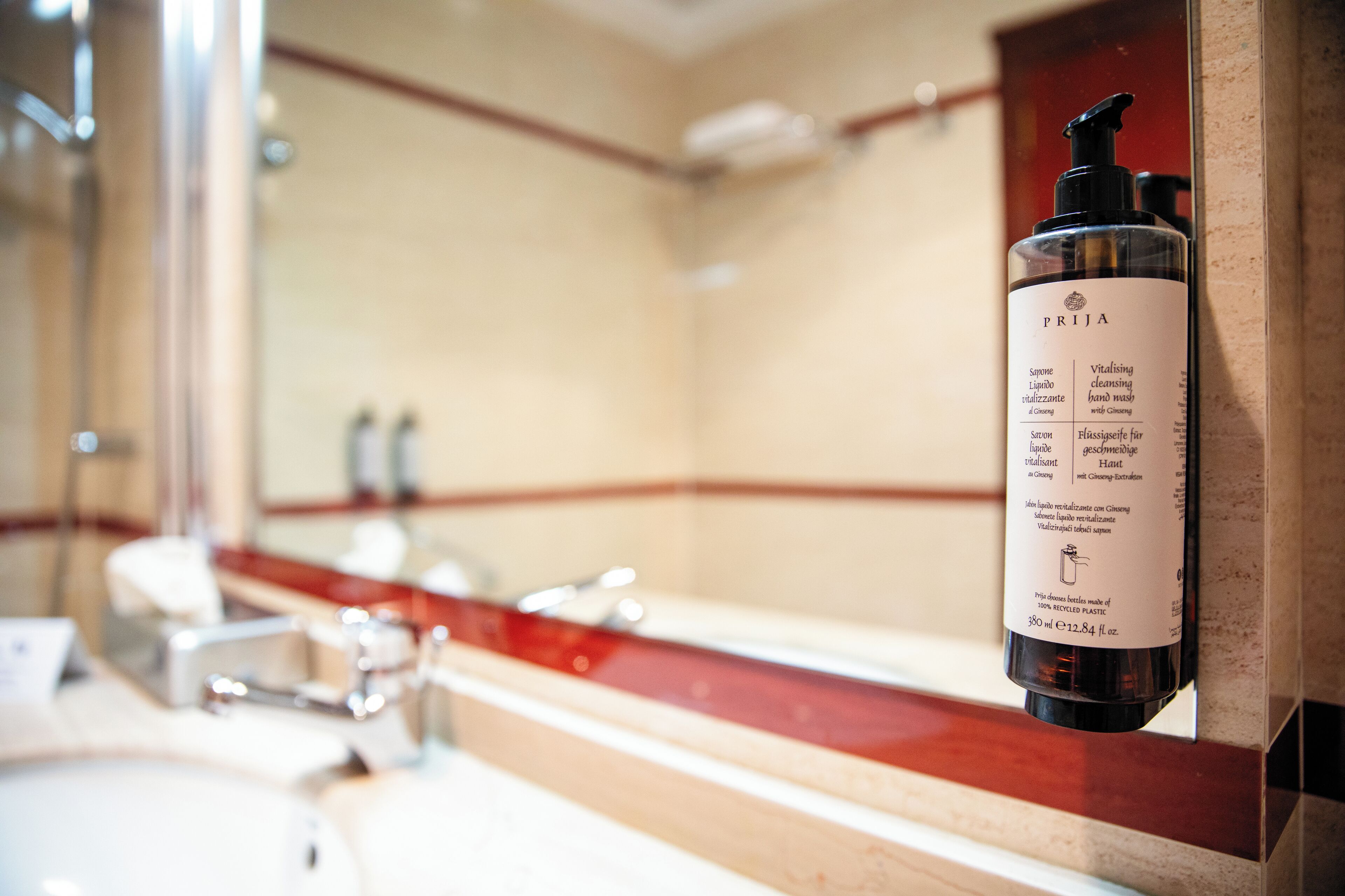 A bathroom with a mirror, sink, and a bottle of PRIJIA hand wash.