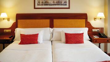 Una cama doble con sábanas blancas y almohadas rojas, dos mesitas de noche con lámparas y un cuadro en la pared.