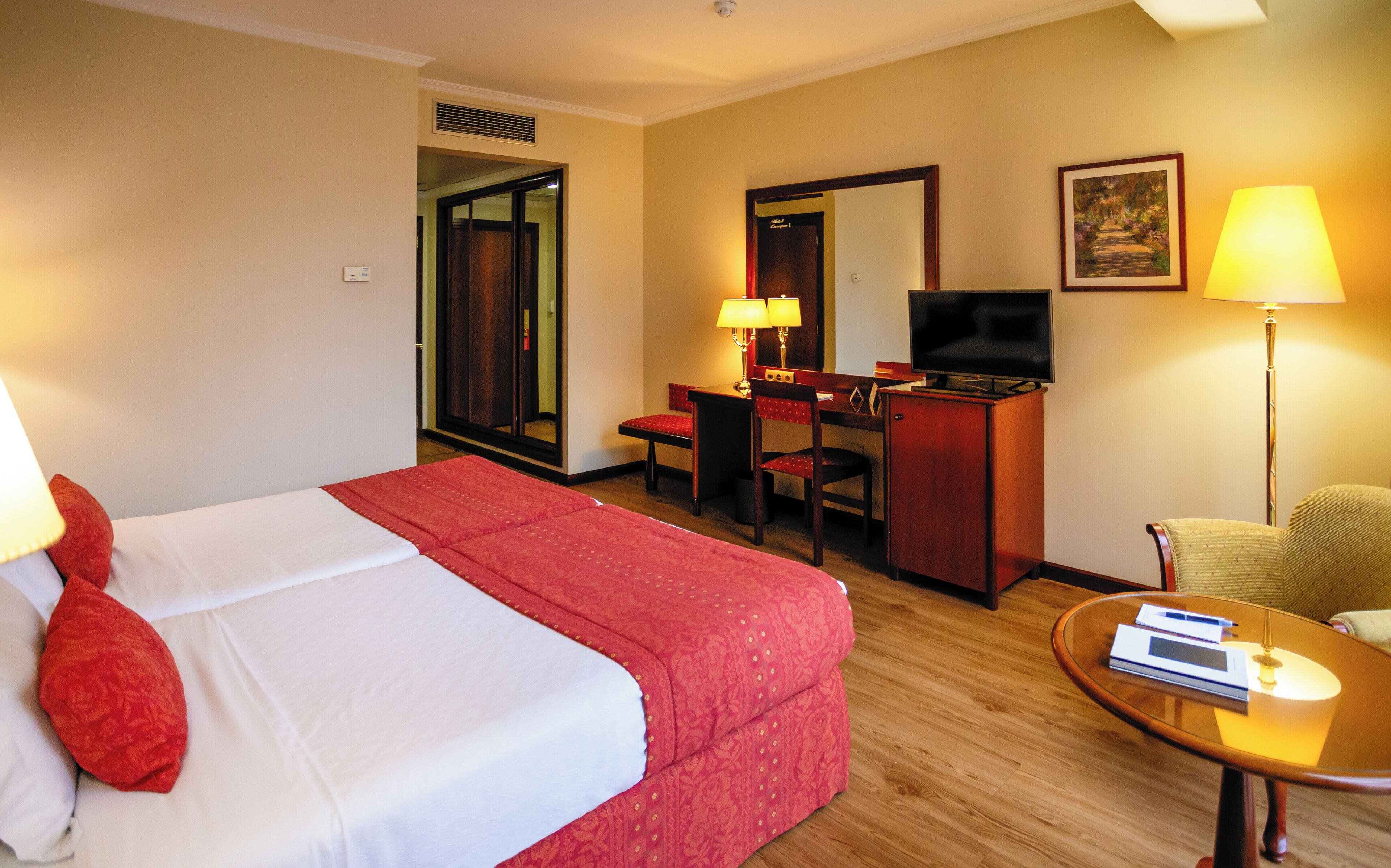 A hotel room with a bed, desk, chair, television, and a lamp.