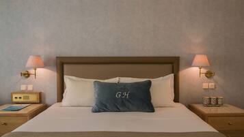 A neatly made bed with a pillow featuring initials, bedside lamps, a radio, and a small table with cups.