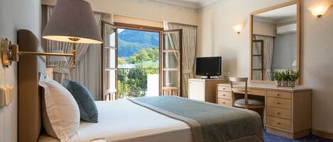 A hotel room with a bed, a desk, a television, and a view of mountains through the window.