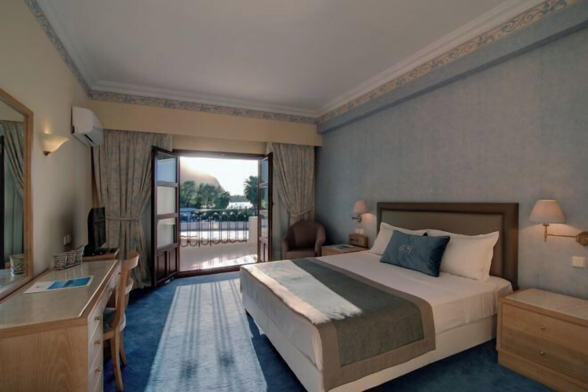 Une chambre d’hôtel avec un lit, des tables de chevet, un bureau et une vue sur l’extérieur, visible à travers une porte vitrée.