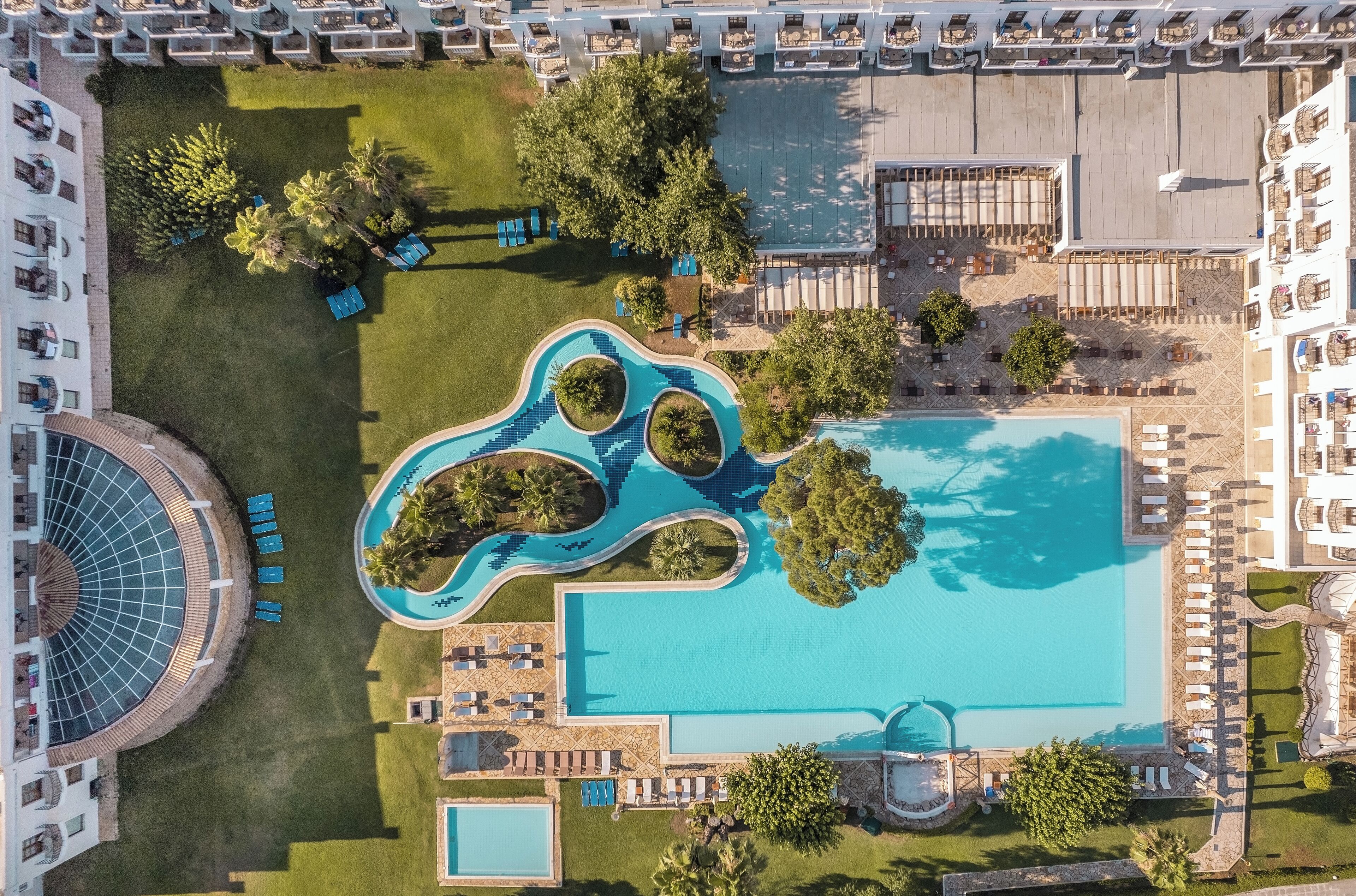 Vista aérea de un hotel con una piscina grande, tumbonas y una estructura circular.