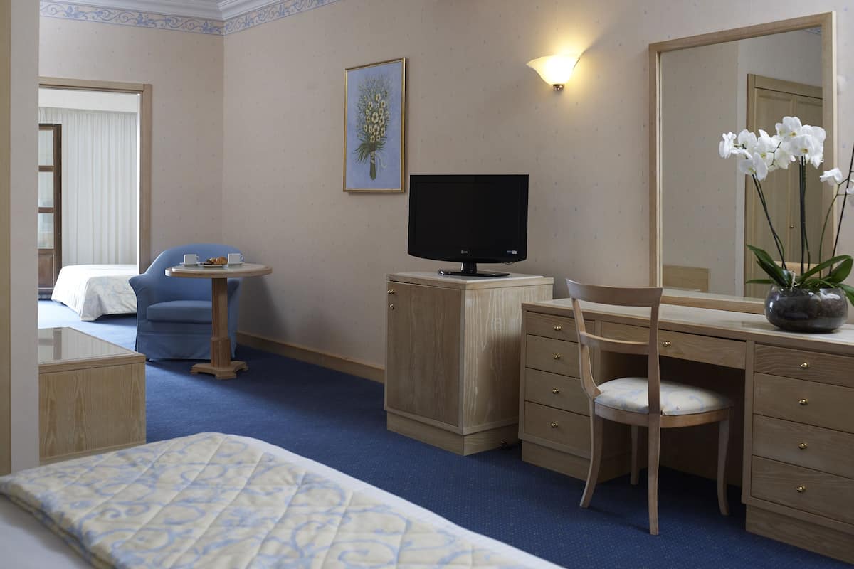 Ein Hotelzimmer mit einem Bett, einem Schreibtisch mit Computer, einem Stuhl, einem kleinen Tisch mit Tasse und Teller, einem Bild an der Wand und einem großen Spiegel.